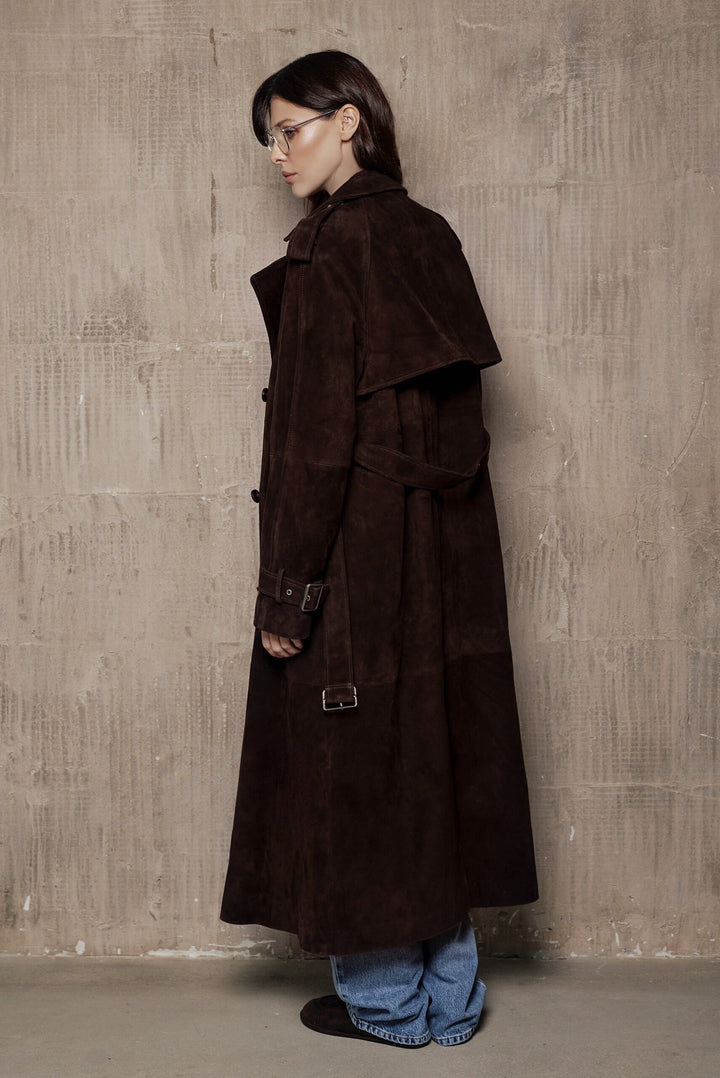 A woman dressed in a rich suede leather trench coat, showcasing a double-breasted design and a sleek, flattering cut that blends classic style with contemporary appeal.