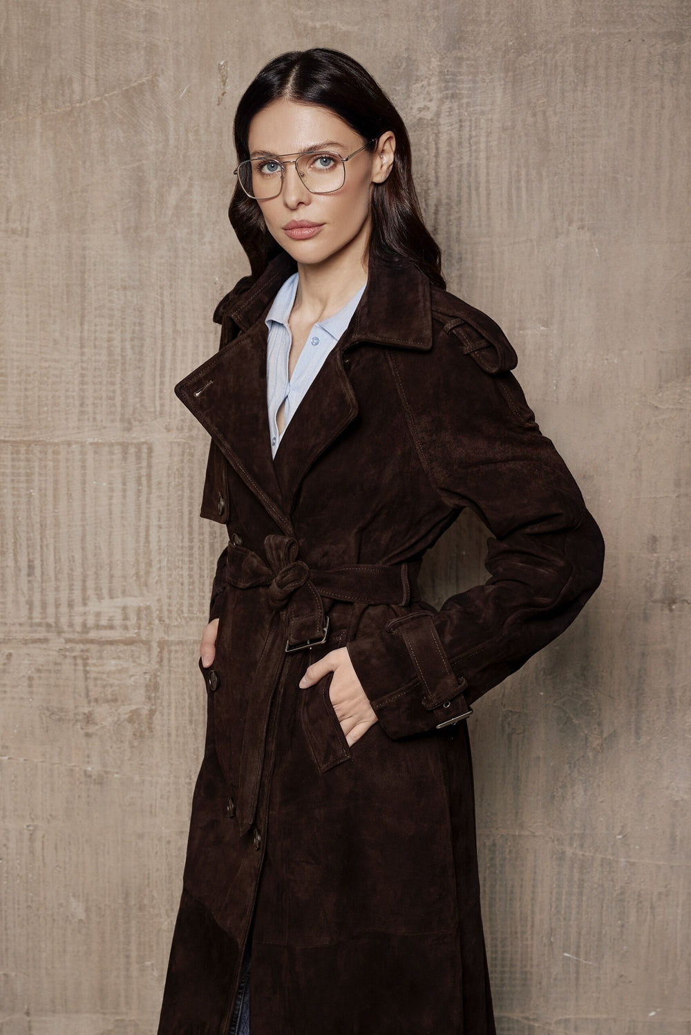 A woman models a sophisticated dark brown suede trench coat, featuring a classic double-breasted design and figure-enhancing silhouette in luxurious suede leather.