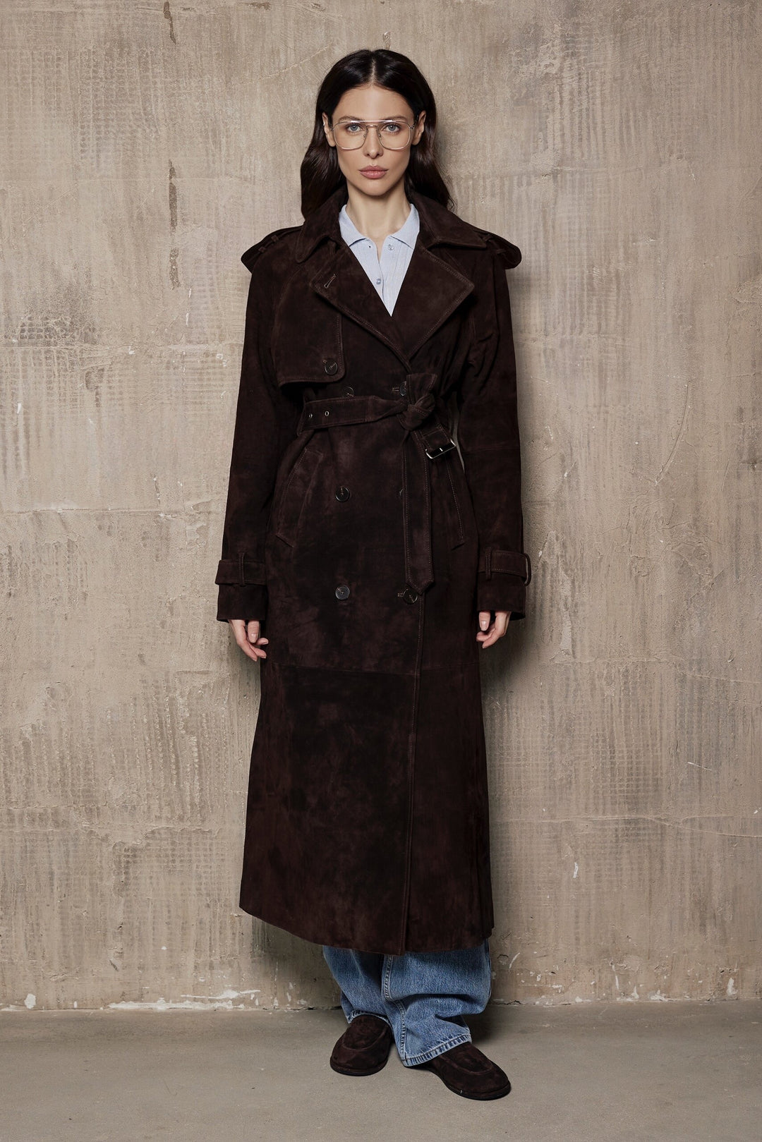 A woman wearing a suede dark brown leather trench coat with a double-breasted front, tailored for a flattering fit and crafted from premium high-quality suede.