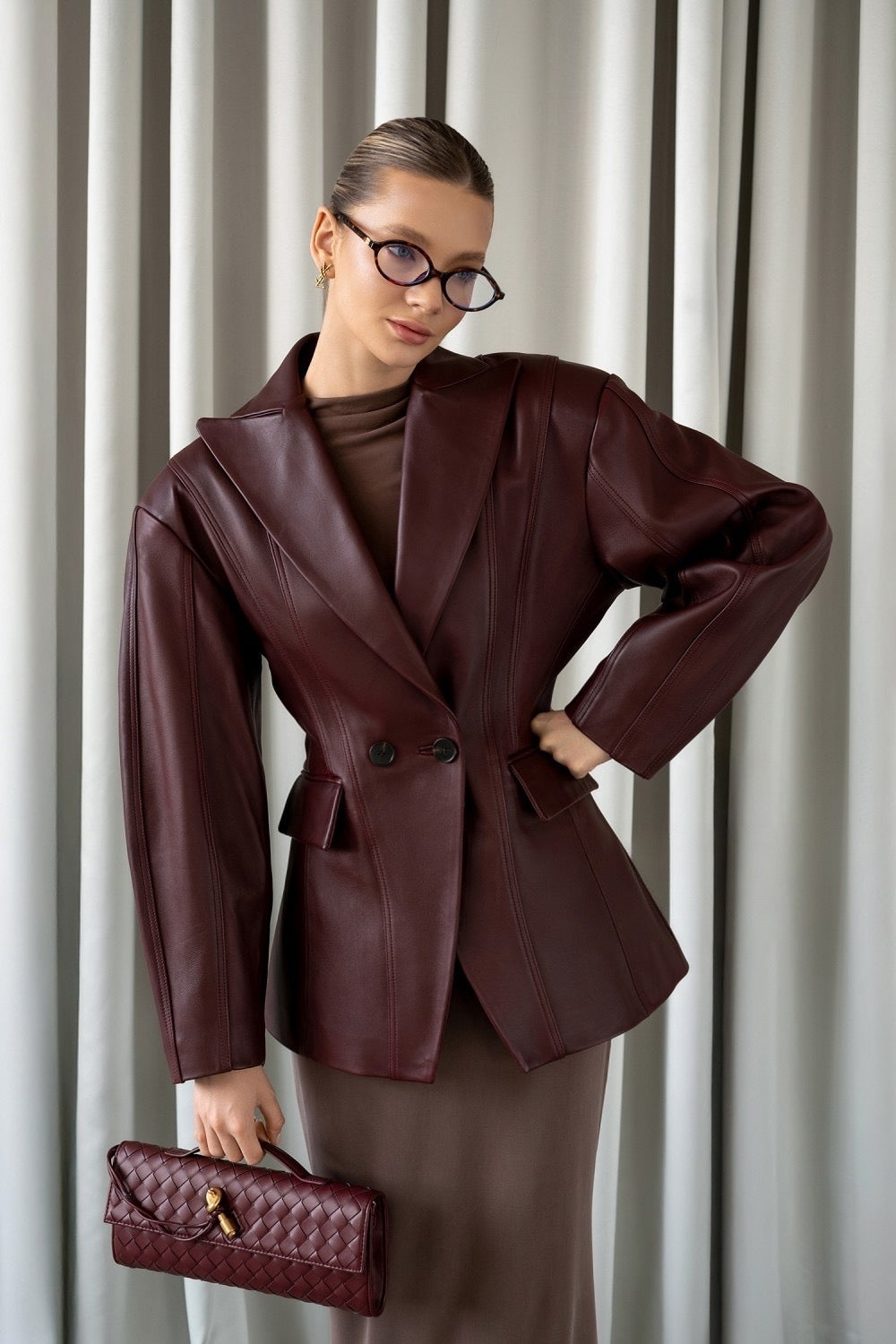 A woman wearing a burgundy leather blazer jacket with a cinched waist, crafted from soft, supple leather for a flattering, elegant silhouette perfect for work or refined casual looks.