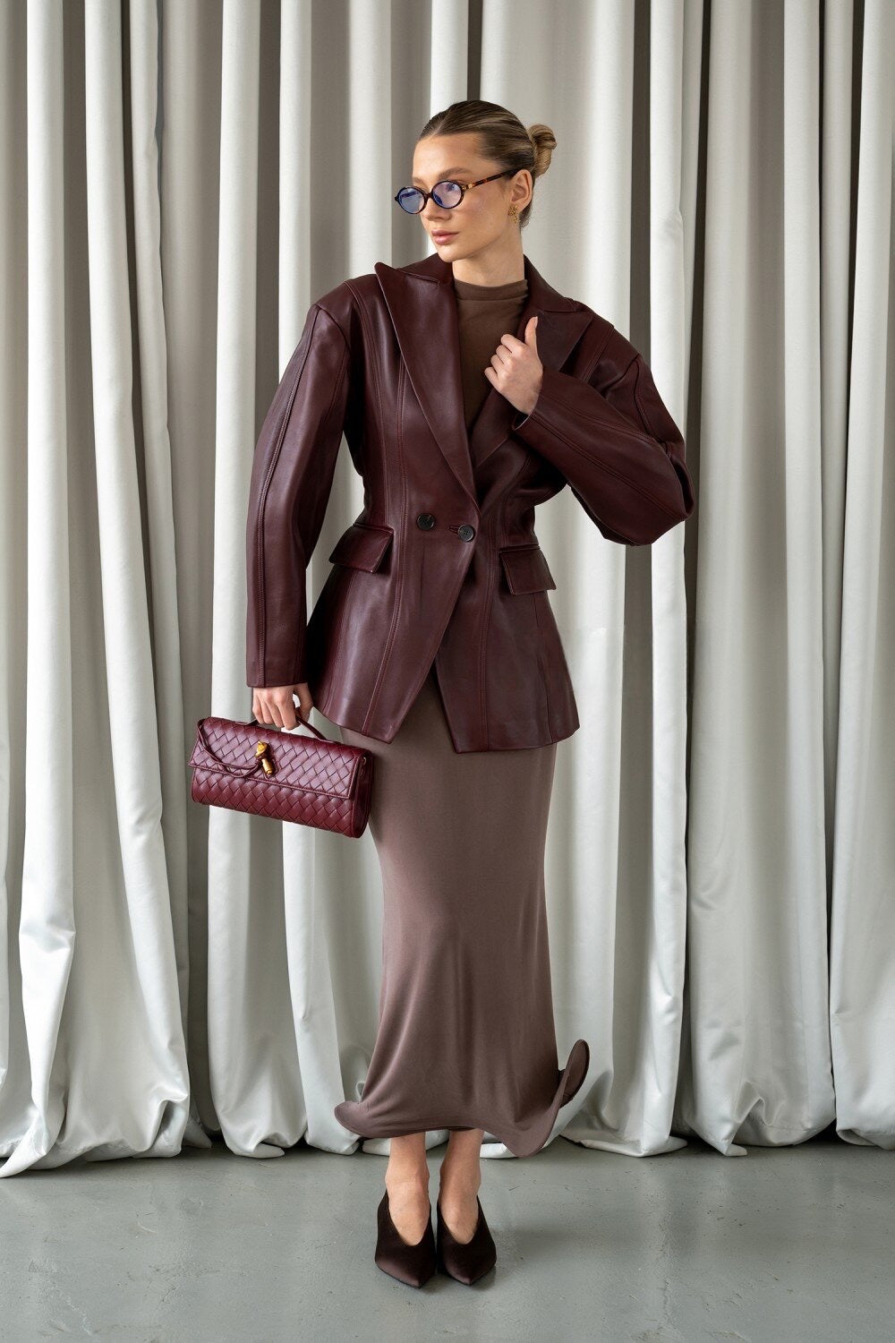 A woman models a tailored burgundy leather blazer featuring a structured fit and feminine waistline, blending sophistication and everyday polish.