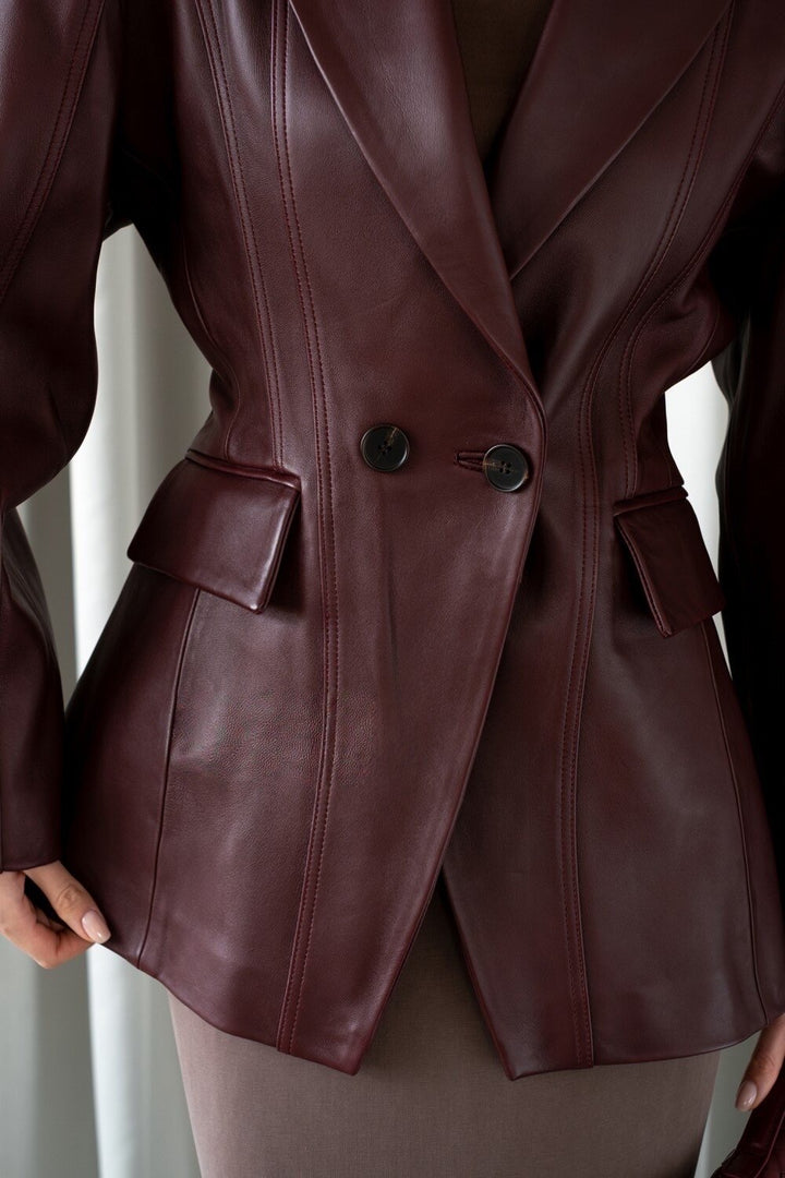A woman dressed in a sleek burgundy leather blazer jacket, showcasing its soft leather texture and cinched design that highlights the feminine shape with timeless appeal.