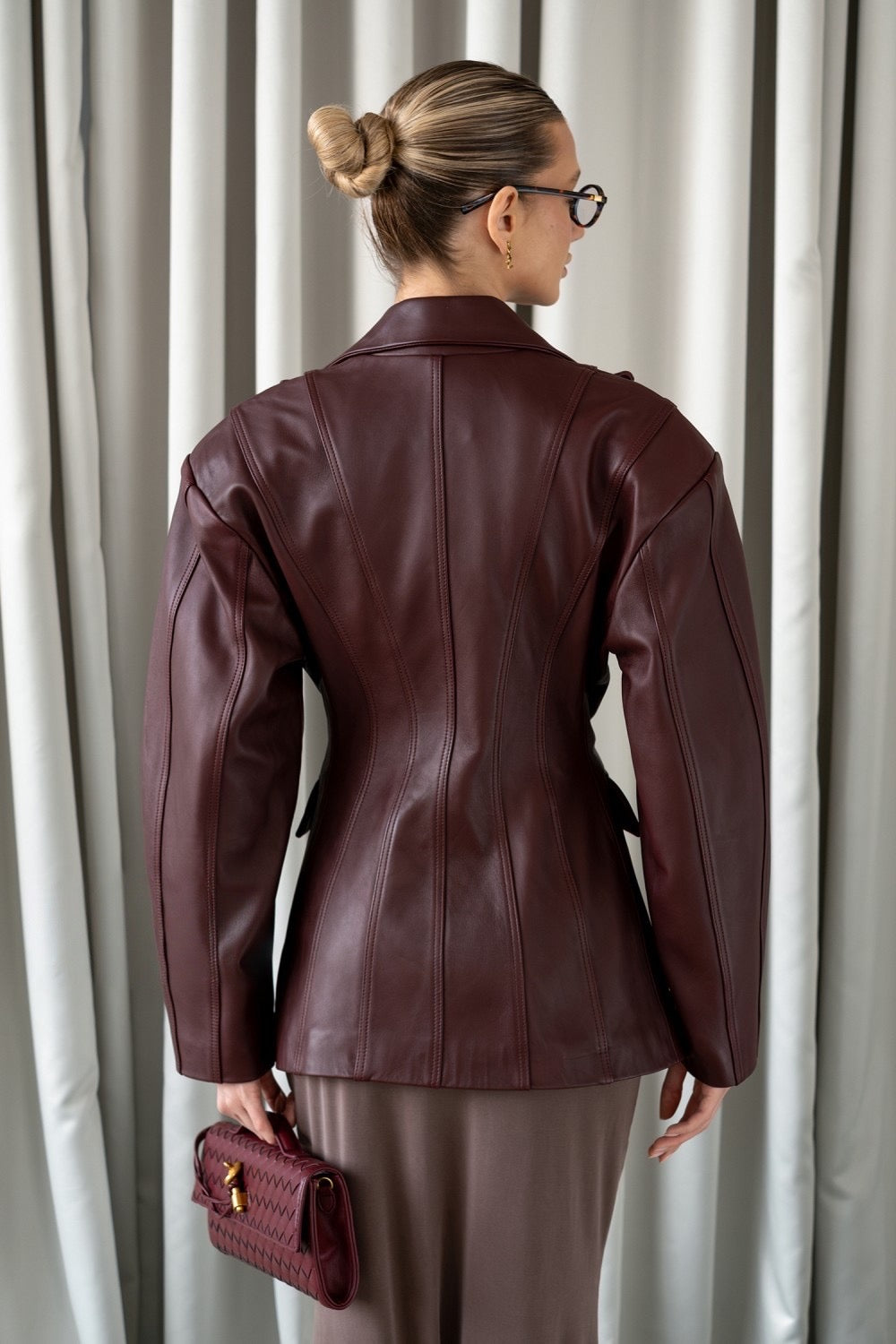 A woman wearing a refined burgundy leather blazer, tailored to accentuate the waist and crafted from supple leather for a chic, versatile look ideal for both professional and casual settings.
