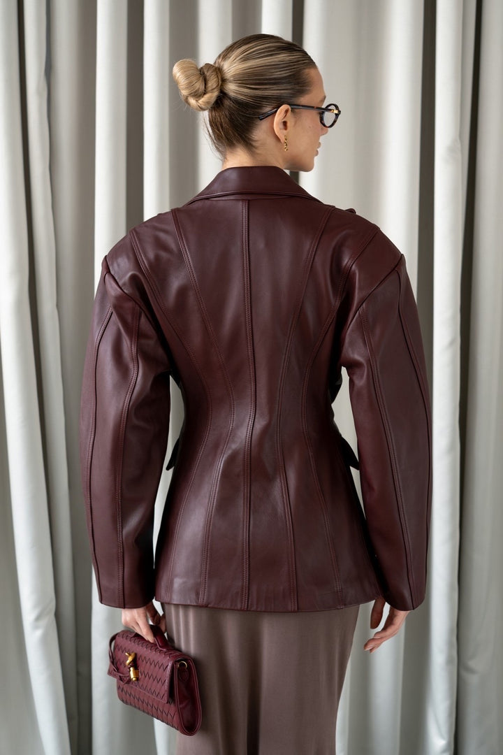 A woman wearing a refined burgundy leather blazer, tailored to accentuate the waist and crafted from supple leather for a chic, versatile look ideal for both professional and casual settings.