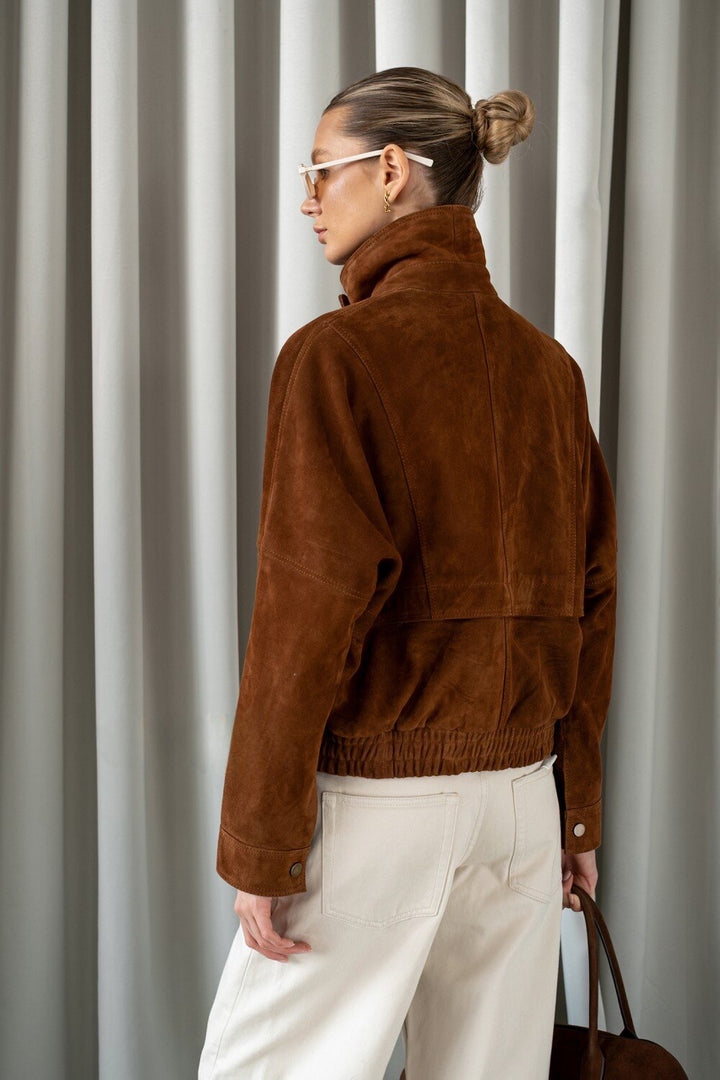 Sophisticated woman in structured brown suede jacket, showcasing timeless outerwear with a contemporary silhouette.