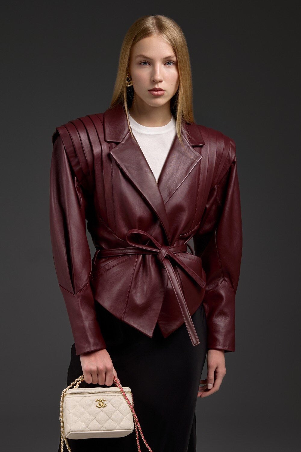 A woman wearing a burgundy genuine leather jacket crafted from soft lambskin, featuring a sleek tailored fit, bold lines, and modern detailing for a refined yet edgy look.
