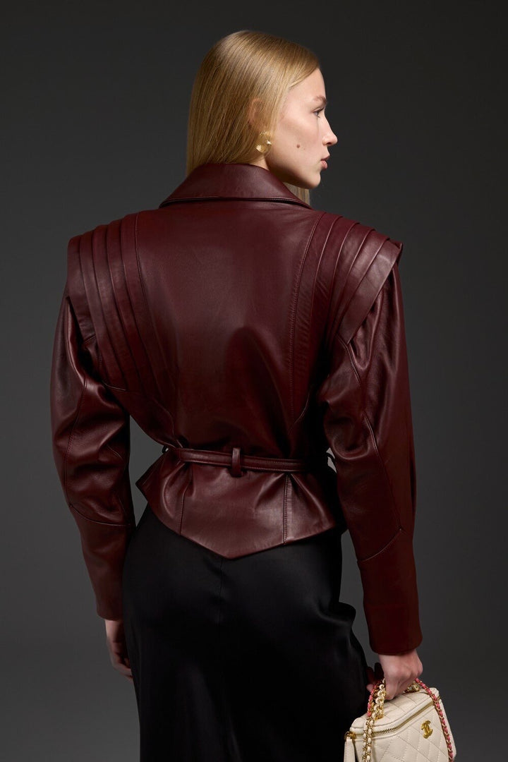 A woman dressed in a high-quality burgundy leather jacket, showcasing its soft lambskin texture, sharp tailoring, and distinctive design elements that elevate it beyond a classic cut.