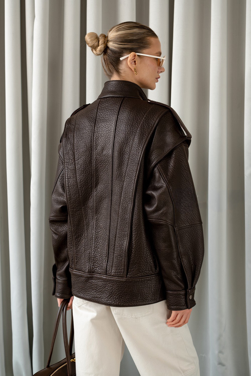 A woman models a tailored dark brown leather jacket, highlighting its warm tone and timeless appeal.