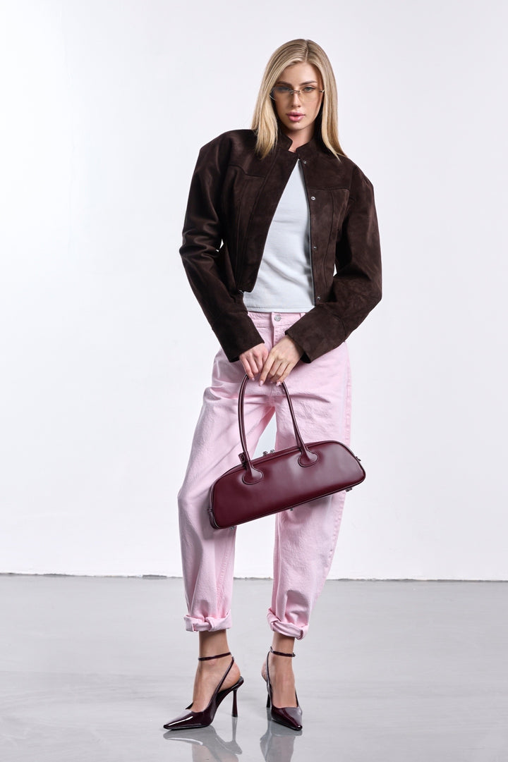A woman wearing a tailored suede jacket in a dark espresso tone, featuring a high collar and a sculpted fit that emphasizes a sharp, minimalist silhouette.