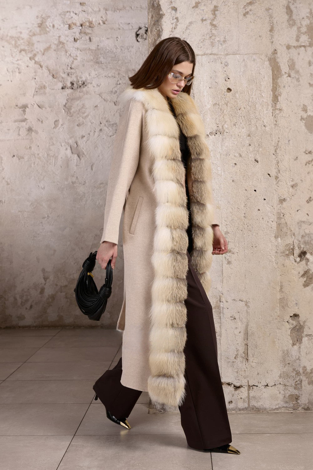 A woman models a luxurious beige coat crafted from double-faced cashmere, highlighted by a cascading genuine gold fox fur trim and a refined belt at the waist.