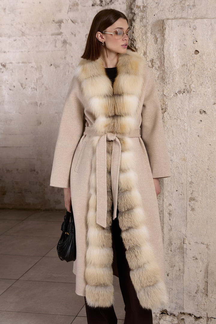 A woman dressed in a beige cashmere coat with clean lines and a flattering fit, adorned with soft gold fox fur along the front for added warmth and sophistication.