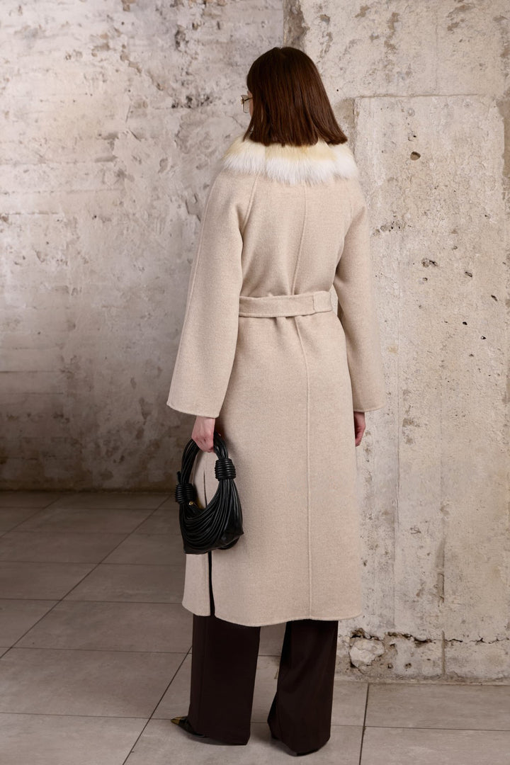A woman wearing a tailored beige coat made from 100% cashmere, complete with a belted waist and rich gold fox fur trim for a timeless and elegant winter style.