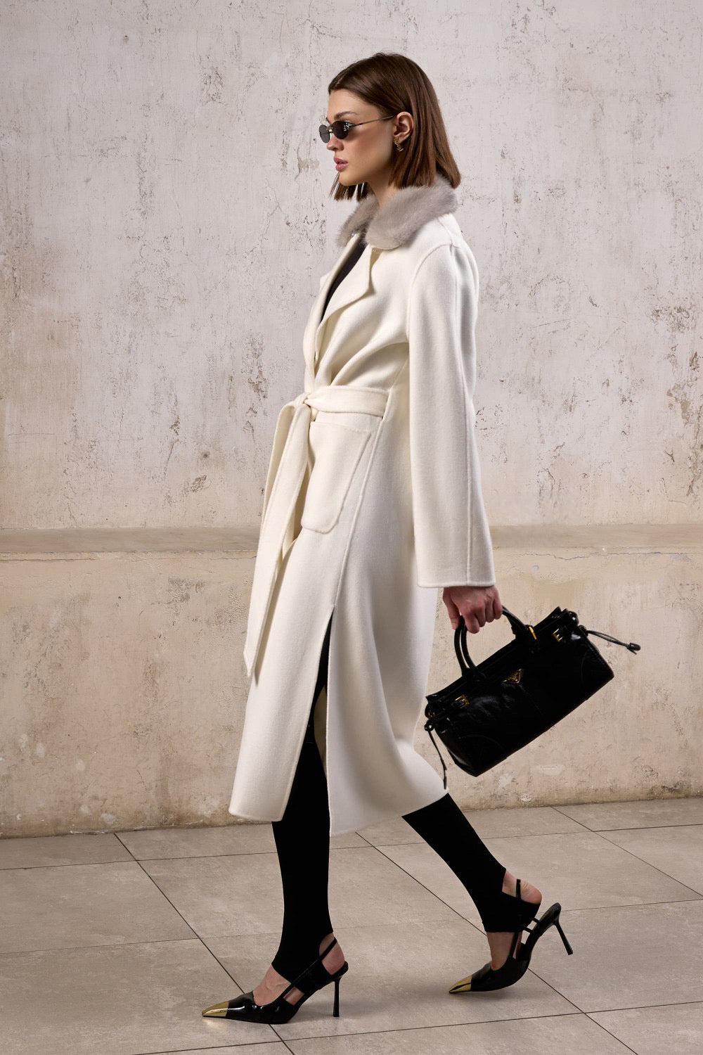 A woman in a chic, relaxed-fit cashmere coat featuring a striking contrast mink collar in grey, exuding comfort and understated elegance.