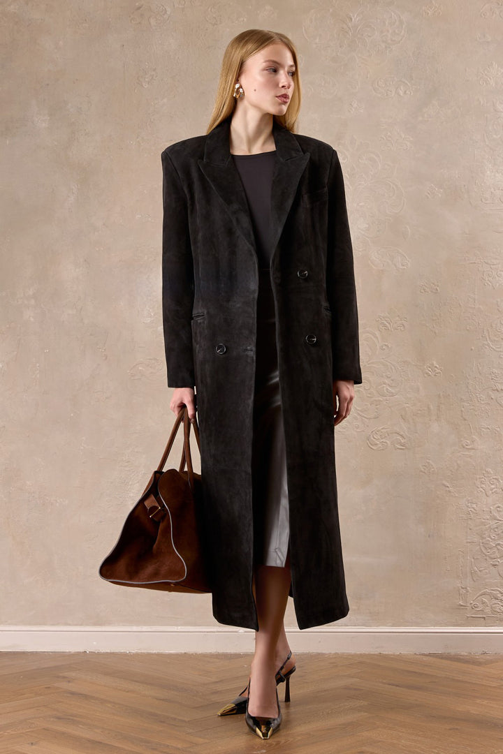 A woman models a premium dark brown suede coat, complete with sharp shoulders and a belted waist for a sophisticated, commanding look.