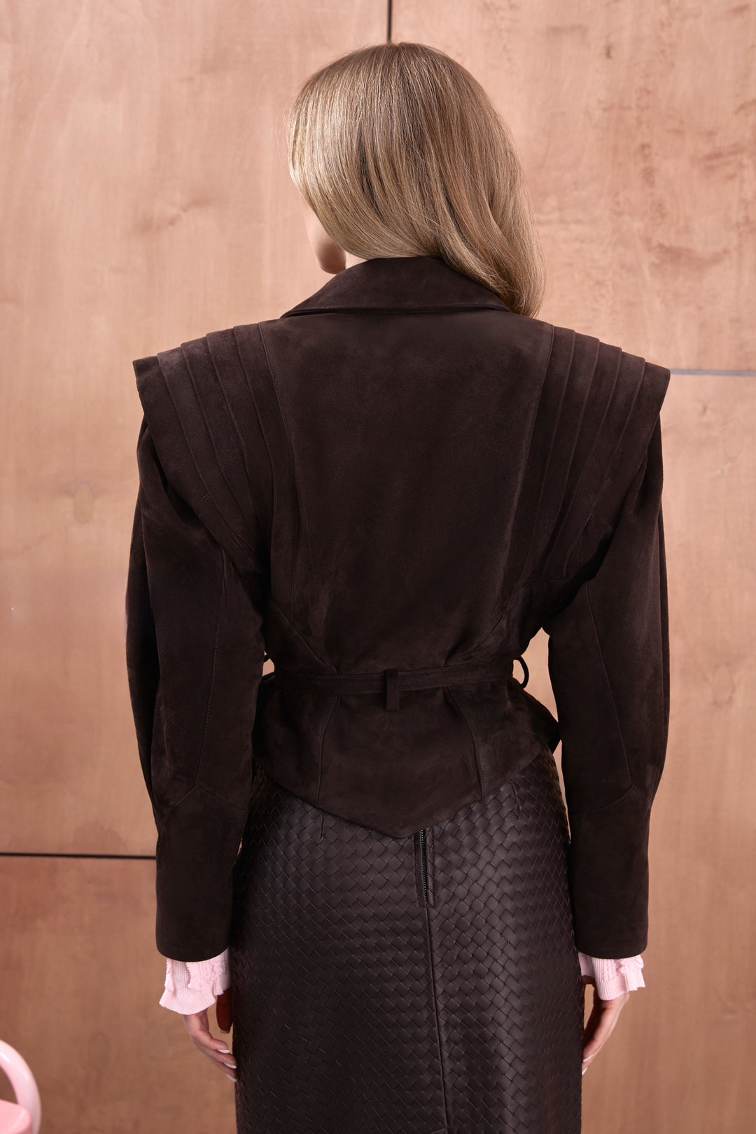 A woman wears a dark brown ultra-stylish suede leather jacket, showcasing a modern tailored fit with rich texture and sophisticated detailing.
