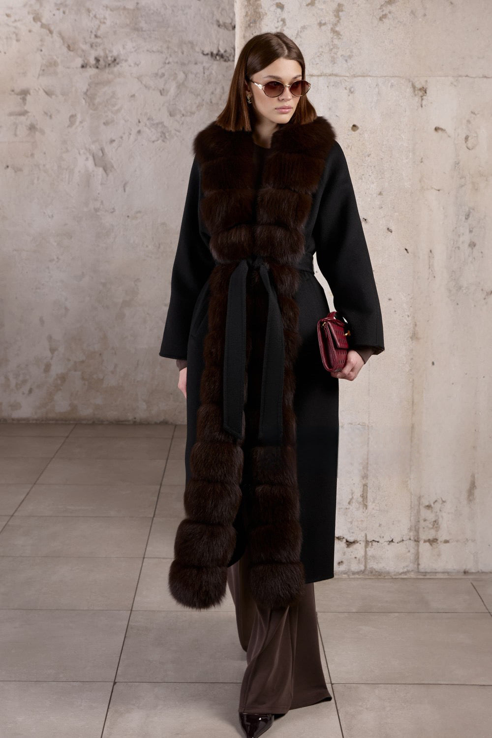 A woman wears an elegant black double-faced cashmere coat with a rich brown fox fur trim, exuding timeless sophistication and grace.