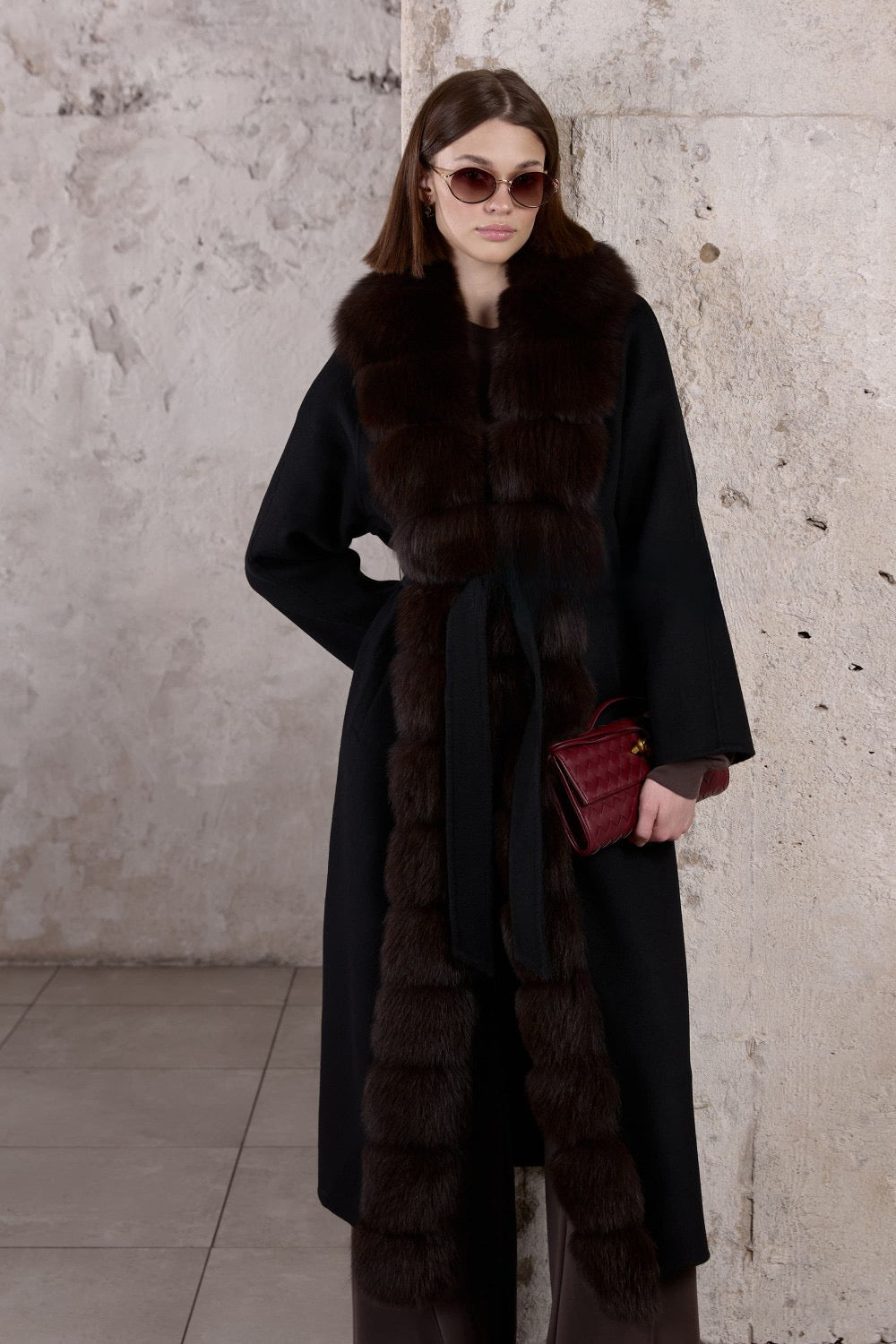 Dressed in a tailored black cashmere coat with cascading brown fox fur, a woman showcases refined winter elegance and warmth.
