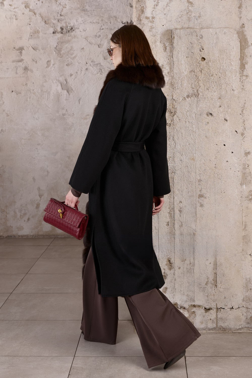 In a black cashmere coat with a lavish brown fox fur front, a woman presents an effortlessly chic and sophisticated winter look.