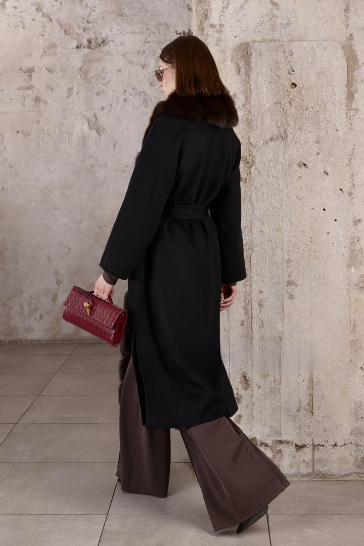 In a black cashmere coat with a lavish brown fox fur front, a woman presents an effortlessly chic and sophisticated winter look.