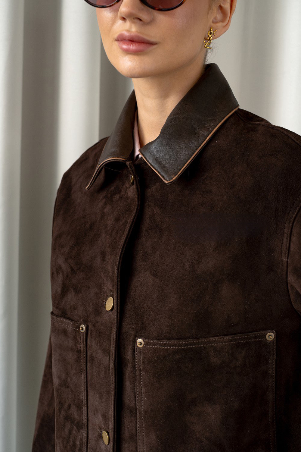 Close up from a brown suede leather jacket with front flap pockets and a lapelled collar, combining depth, sophistication, and modern style.