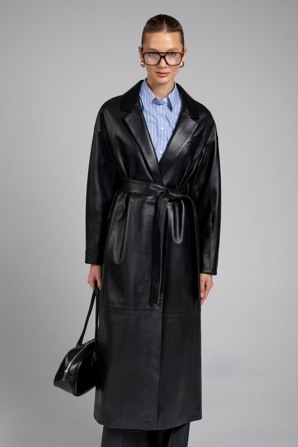 Styled in wide trousers and carrying a black leather bag, the woman showcases a premium genuine leather coat with a double-breasted front and sharply tailored silhouette.