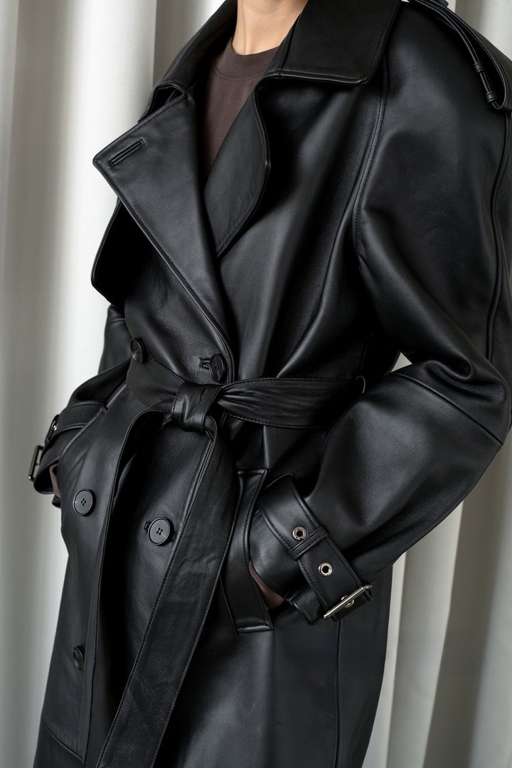 Close up from a genuine black leather trench coat, combining timeless double-breasted style with buttery soft leather and refined belted cuff details.