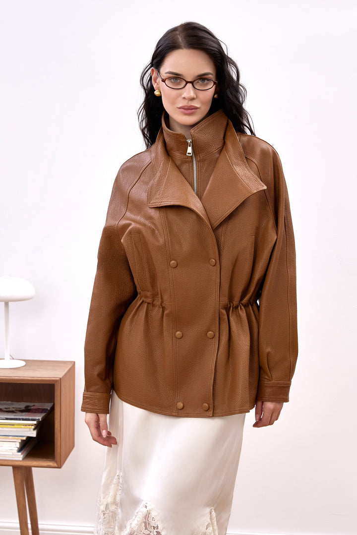 A woman wears the Simona Genuine Leather Jacket very elegantly, showcasing its sporty yet chic design with a high neck and relaxed fit.
