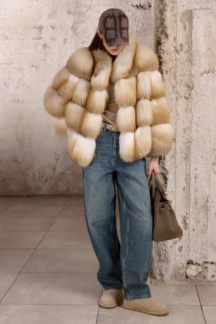 A woman pairs her denim jeans with a voluminous Gold Fox Fur Coat, the rich tones of the fur contrasting stylishly with her casual look.