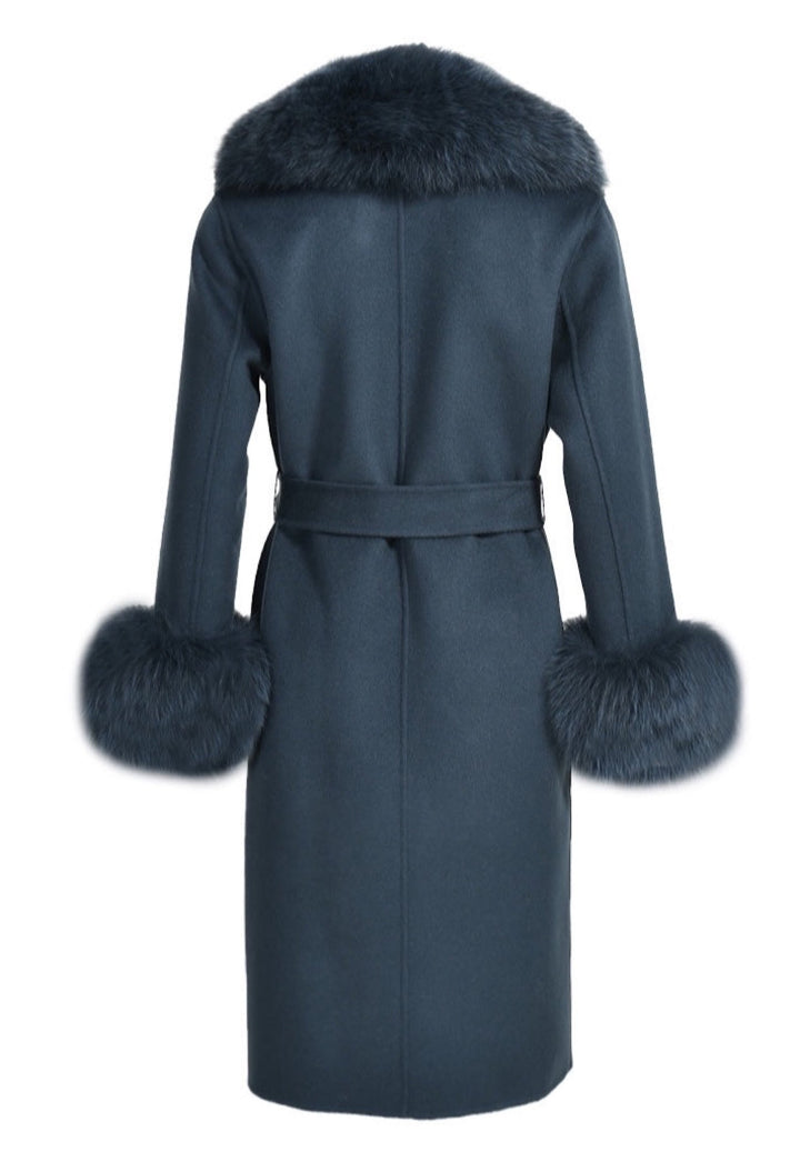 An Aegean blue cashmere coat with plush fox fur trim envelops the woman in elegance. The vivid blue shade and high-quality fur elevate her cold-weather ensemble.